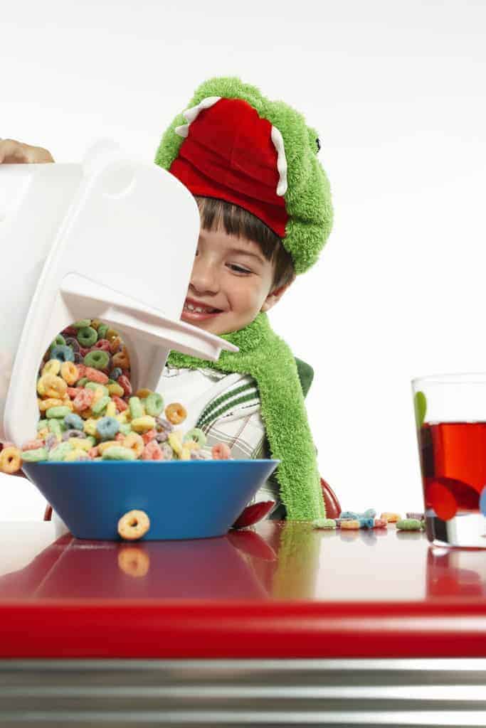 A boy pouring a large bowl of sugary cereal.