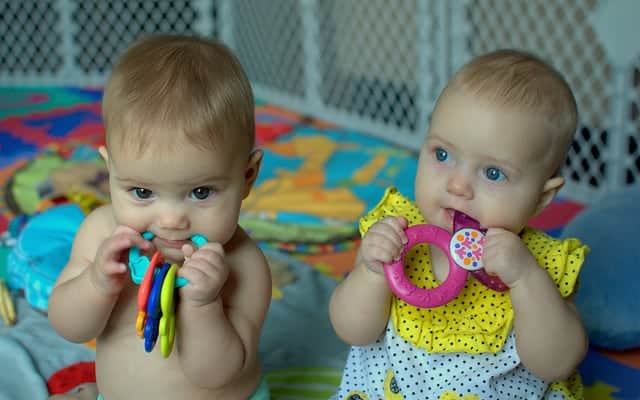 Two babies teething on teething rings. Teething causes pain and may be a reason your baby refuses to eat.