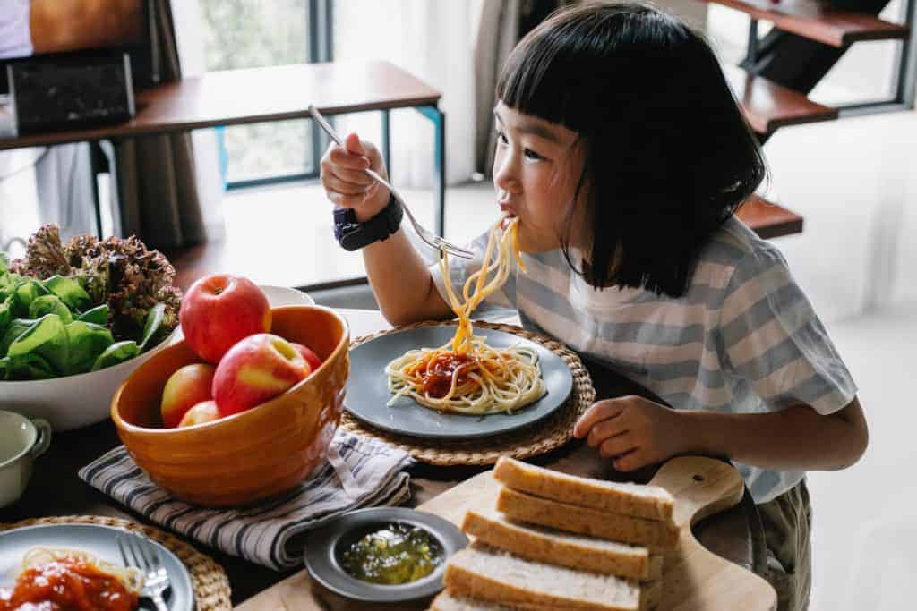 Little girl eating a family-style meal with pasta.