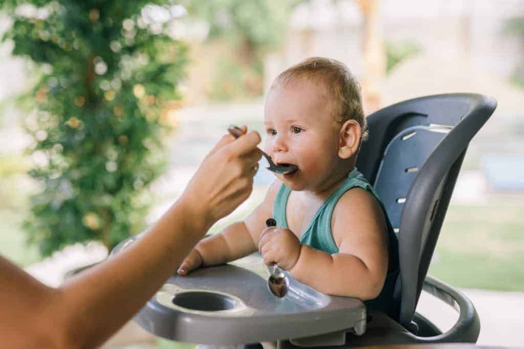 Baby in a highchair eating baby food.